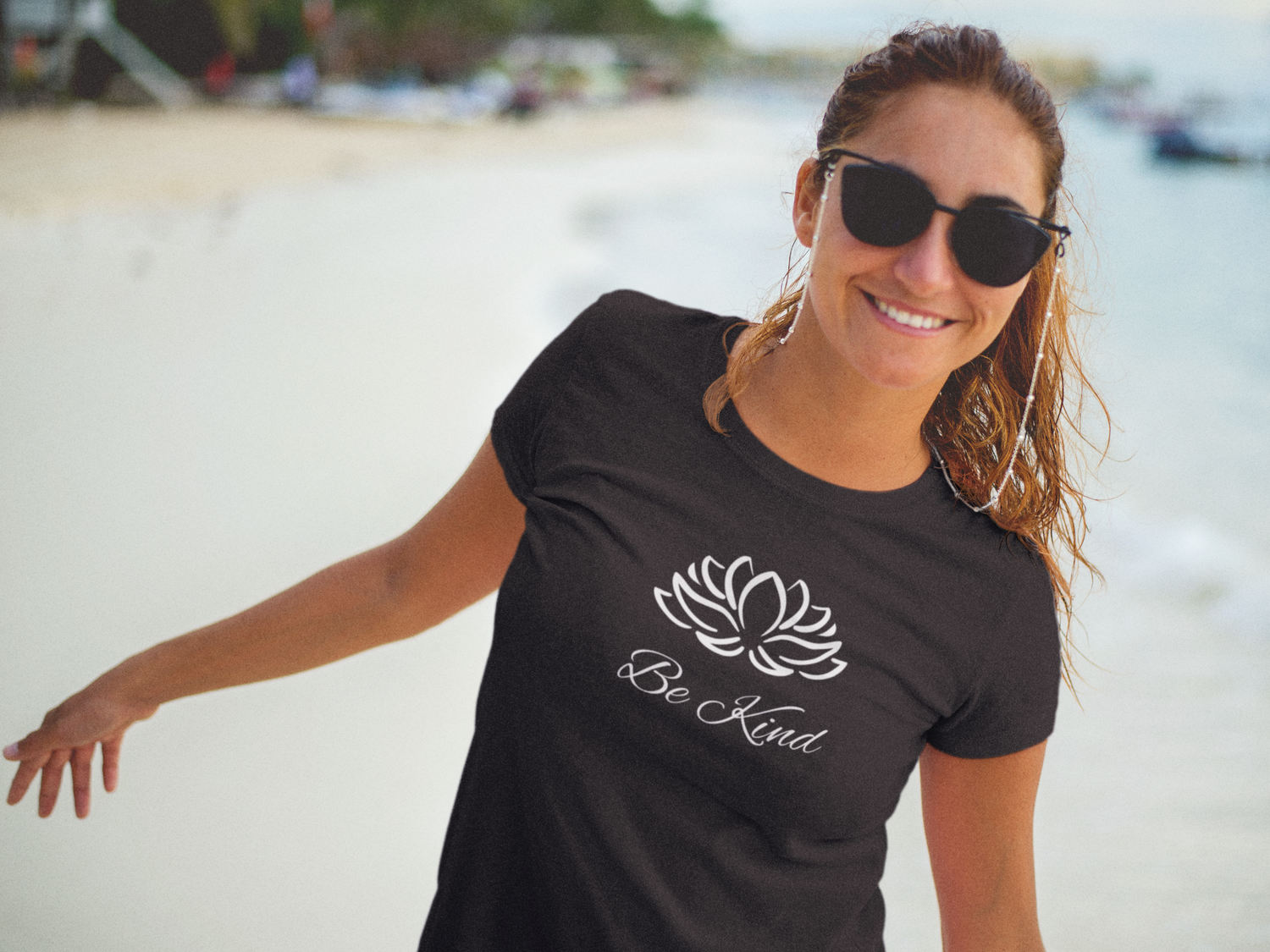 Woman on the beach wearing a t-shirt with a lotus flower that says Be Kind